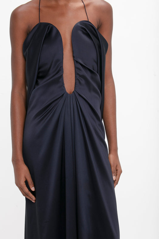 Woman wearing an elegant navy blue evening gown crafted from crepe back satin, featuring a halter neckline with a keyhole cutout, focusing on the upper part of the dress and torso by Victoria Beckham.