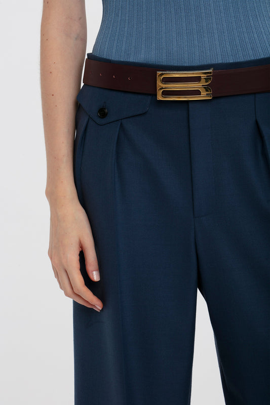 Close-up of a woman wearing Victoria Beckham navy blue wide leg cropped trousers with a brown belt and a light blue fine knit tank, focusing on her waist and hips.
