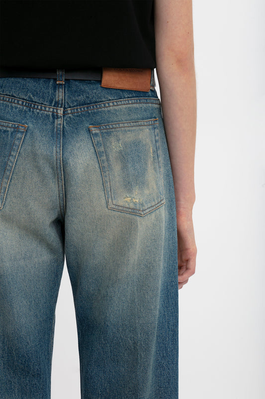 Close-up of a person wearing Victoria Beckham Relaxed Straight Leg Jean In Antique Indigo Wash showing a detailed view of the back pocket and waistband against a white background.