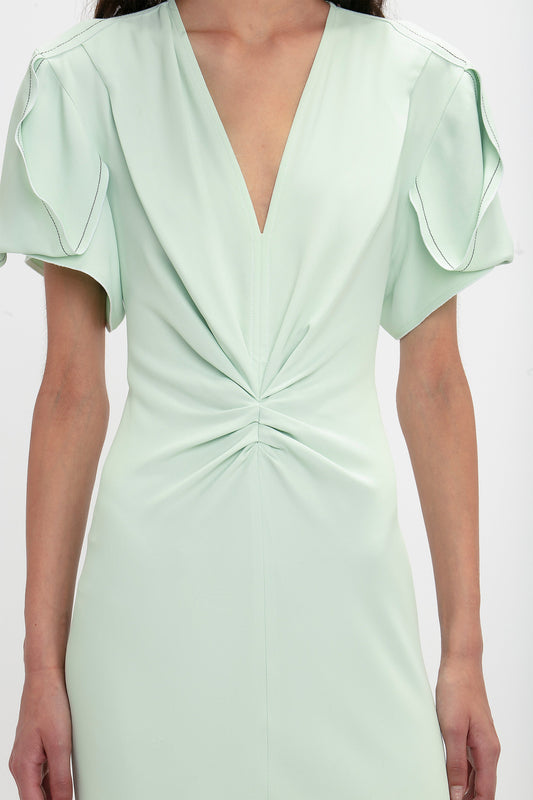 Close-up of a woman wearing a Victoria Beckham Gathered V-Neck Midi Dress In Jade with short ruffled sleeves and waist-defining pleat detail.
