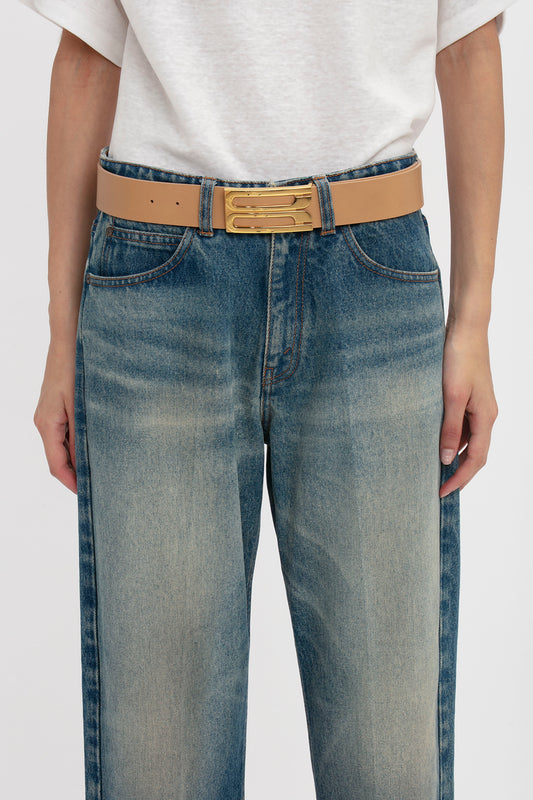Close-up view of a person wearing jeans and a white shirt, with a focus on a Victoria Beckham Jumbo Frame Belt In Camel Leather with gold hardware.