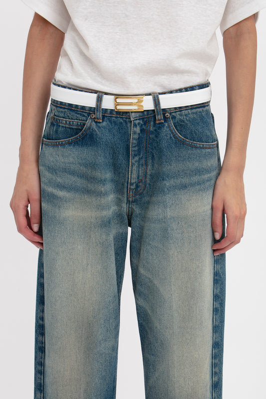 Close-up of a person wearing light-wash jeans and an Exclusive Frame Belt In White Leather with gold hardware by Victoria Beckham, hands resting casually by their sides.