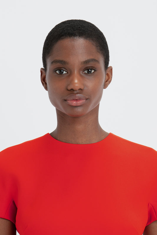 A young black woman with short hair, wearing a Victoria Beckham fitted T-shirt dress in bright red, standing against a plain white background, facing the camera.