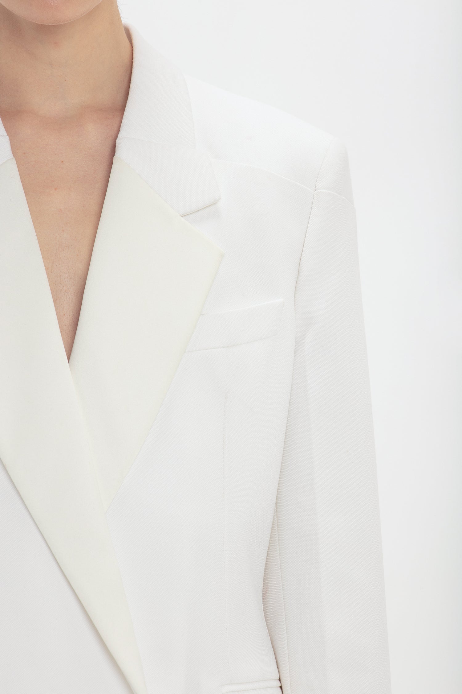 Close-up of a person wearing a white, Victoria Beckham double-breasted cut blazer with a notched lapel, focusing on the details of the collar and chest area.