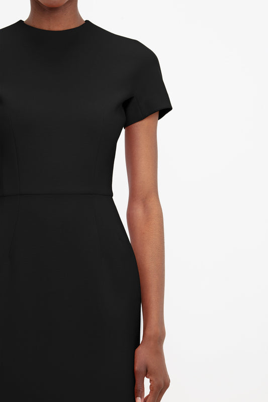 Close-up of a woman in a Victoria Beckham fitted T-shirt dress in black with a simple round neckline and short sleeves, focusing on the upper torso and arm.