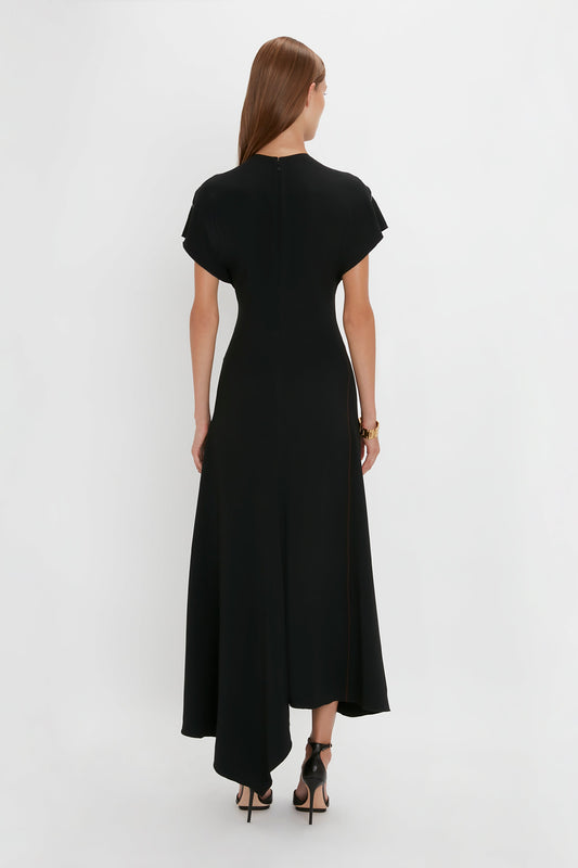 A woman in a Victoria Beckham black crew-neck midi dress with short sleeves and a zipper down the back, standing against a white background.