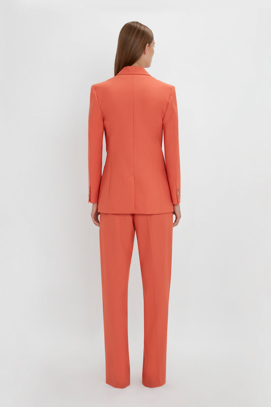 Woman from behind wearing a Victoria Beckham Patch Pocket Jacket in Papaya and trousers, standing against a white background.