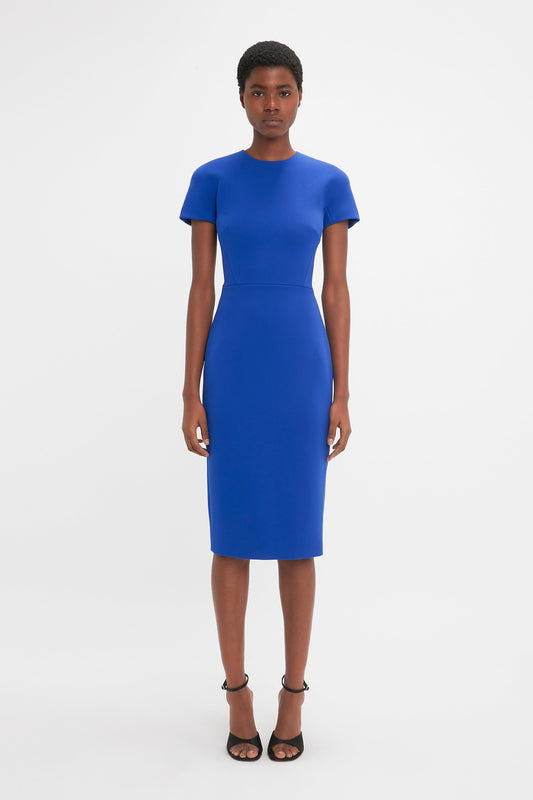 A woman in a Victoria Beckham Palace Blue fitted t-shirt dress and black heels standing against a white background.