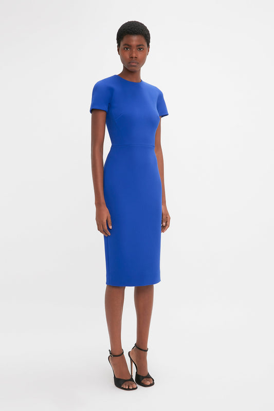 A black woman wearing a Fitted T-Shirt Dress In Palace Blue designed by Victoria Beckham and black heels, standing against a plain white background.