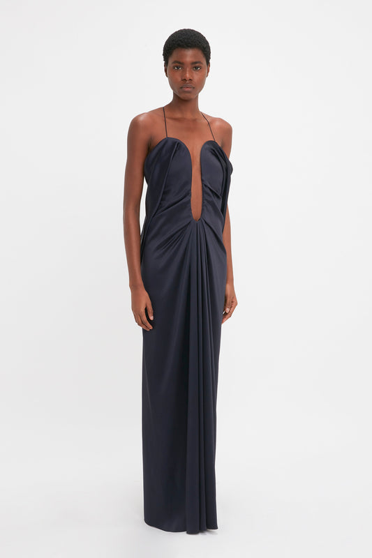A young woman in a navy blue strapless Victoria Beckham Frame Detail Cut-Out Cami Dress, standing against a plain white background.
