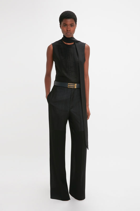 A black woman in a stylish sleeveless black top and Victoria Beckham's Waistband Detail Straight Leg Trousers in Black stands against a plain white background.