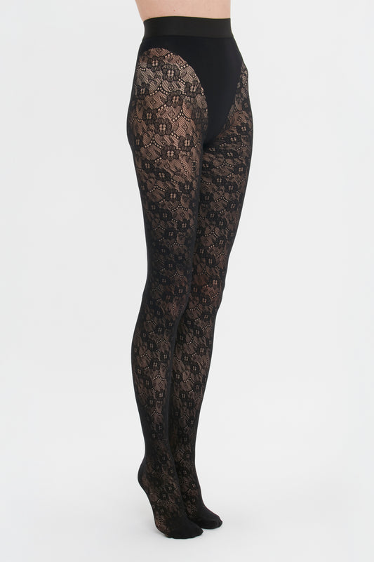 A person standing side-on wearing ornate Victoria Beckham Monogram Lace Tights against a white background.