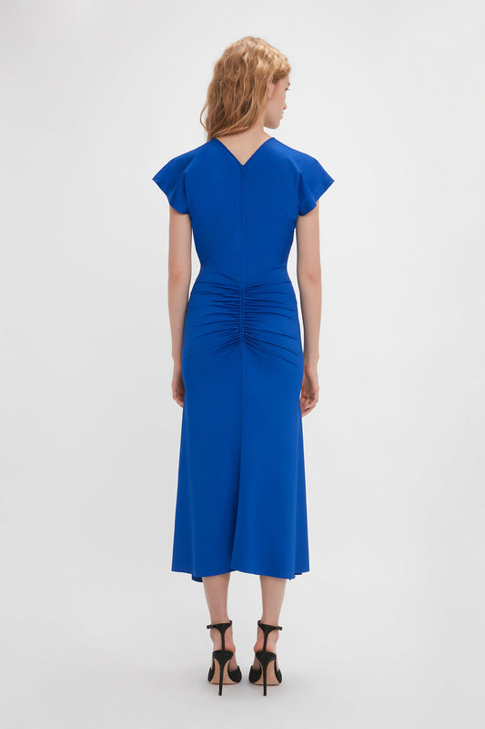 A woman in a Victoria Beckham royal blue Sleeveless Rouched Jersey Dress, standing with her back to the camera against a white background.