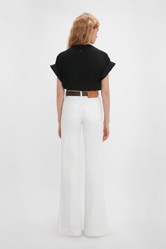 Woman in a Victoria Beckham 'Do As I Say, Not As I Do' Slogan T-Shirt in Black and white wide-leg pants, standing with her back to the camera against a plain background.