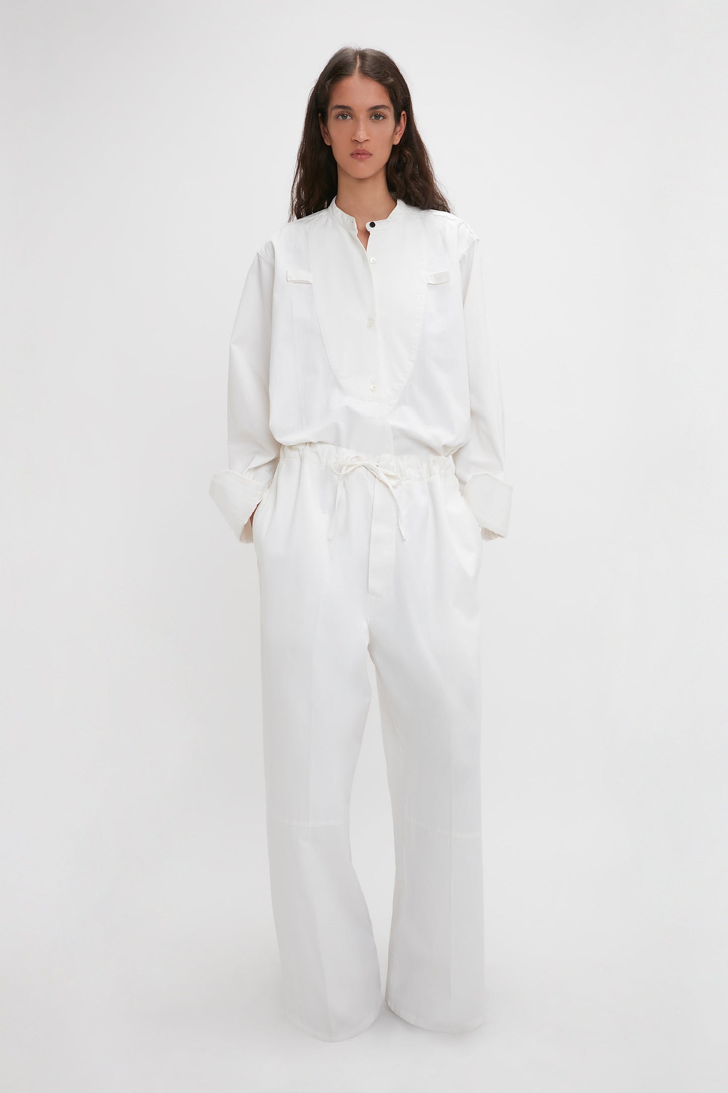 A woman in a white jumpsuit with an adjustable drawstring waistband stands against a plain background. 
    - A woman in Victoria Beckham Drawstring Pyjama Trouser In Washed White stands against a plain background.
