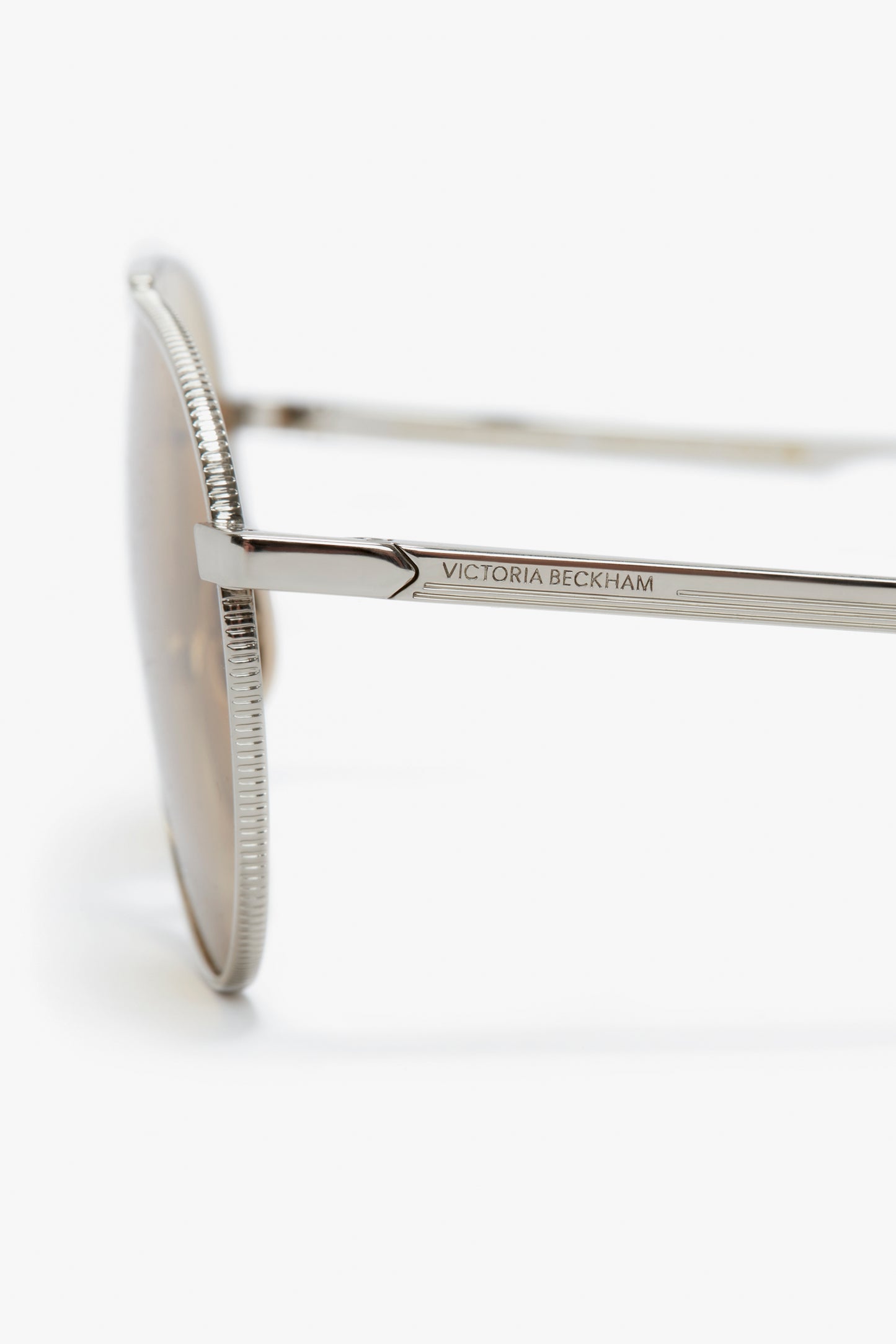 Close-up of the side arm of Victoria Beckham V Metal Pilot sunglasses showing the Victoria Beckham logo on a white background.