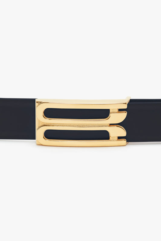 A close-up of a Victoria Beckham Exclusive Frame Belt In Midnight Navy Leather with a shiny gold buckle, featuring a sleek, modern design.