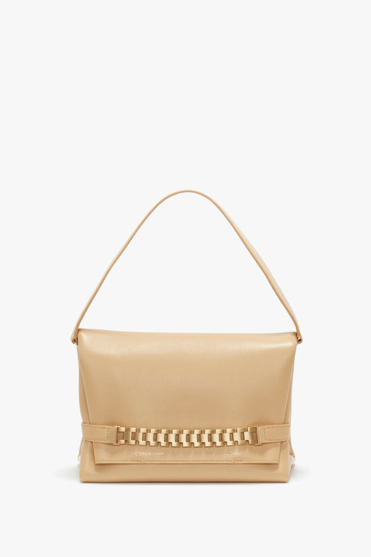 A beige leather crossbody bag with a single top handle and a decorative chain detail on the bottom front, against a white background. Victoria Beckham's Chain Pouch With Strap In Sesame Leather.