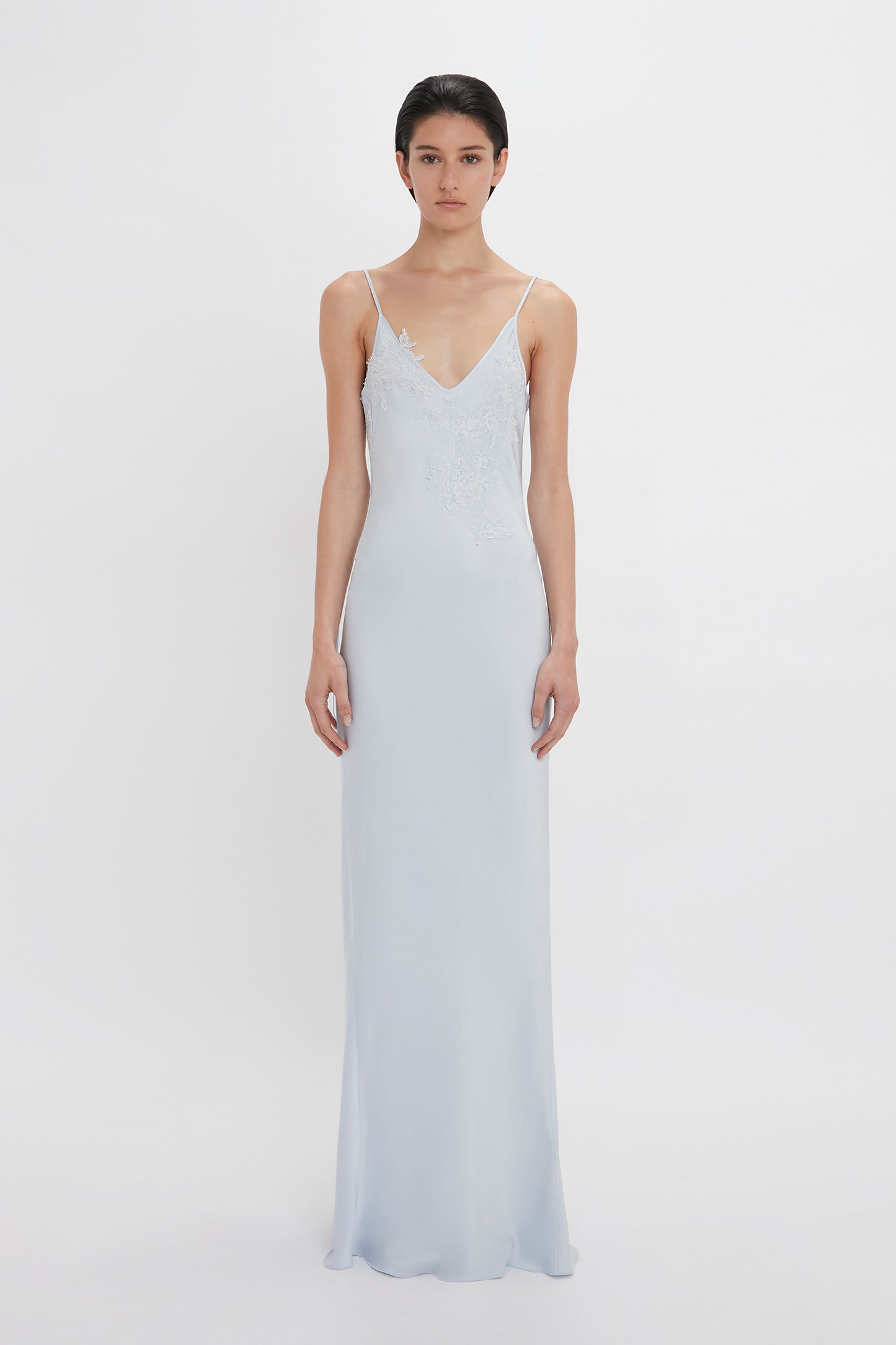 A woman wearing a Victoria Beckham Exclusive Lace Detail Floor-Length Cami Dress In Ice, standing against a white background.