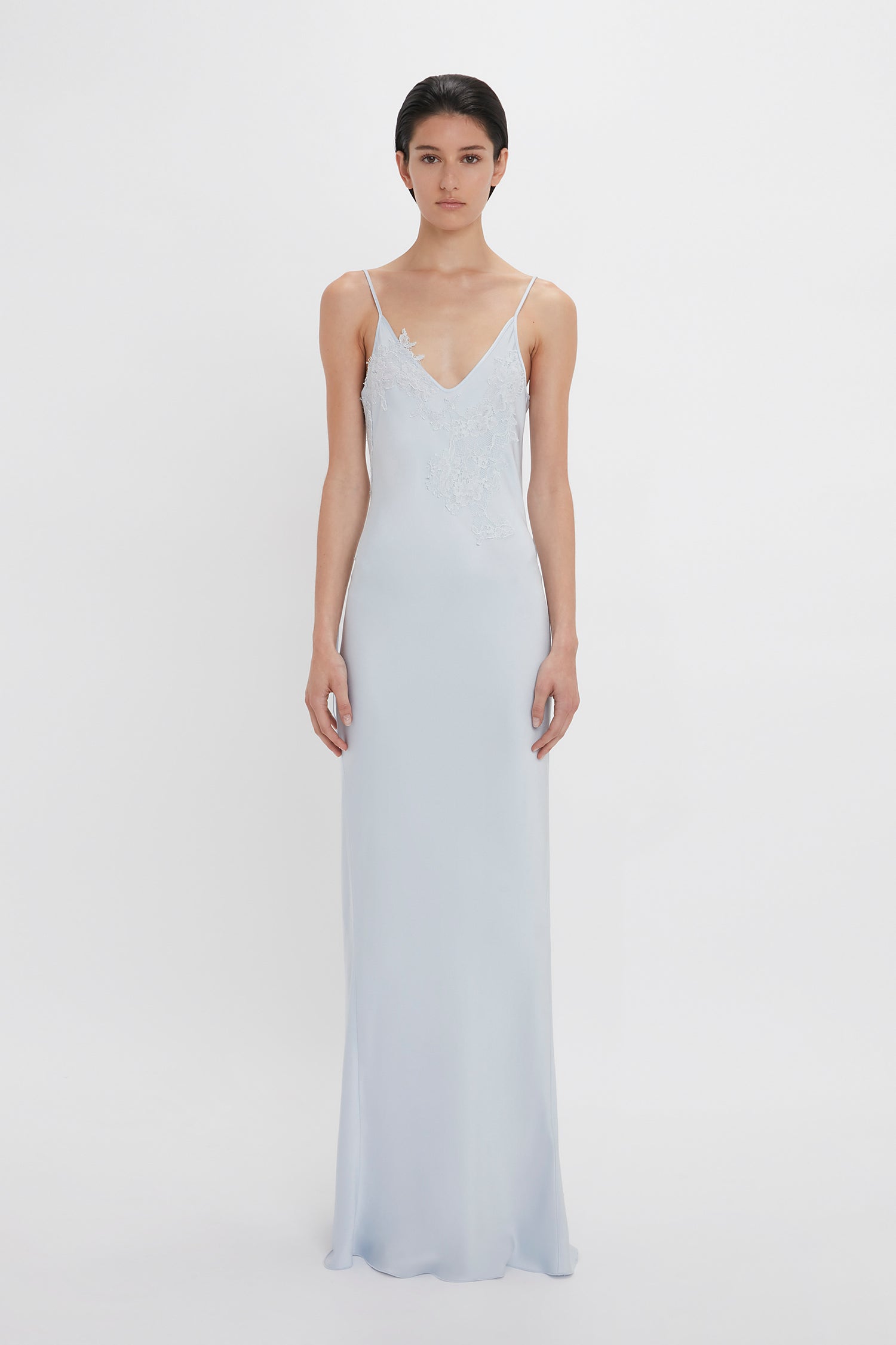 A woman wearing a Victoria Beckham Exclusive Lace Detail Floor-Length Cami Dress In Ice, standing against a white background.