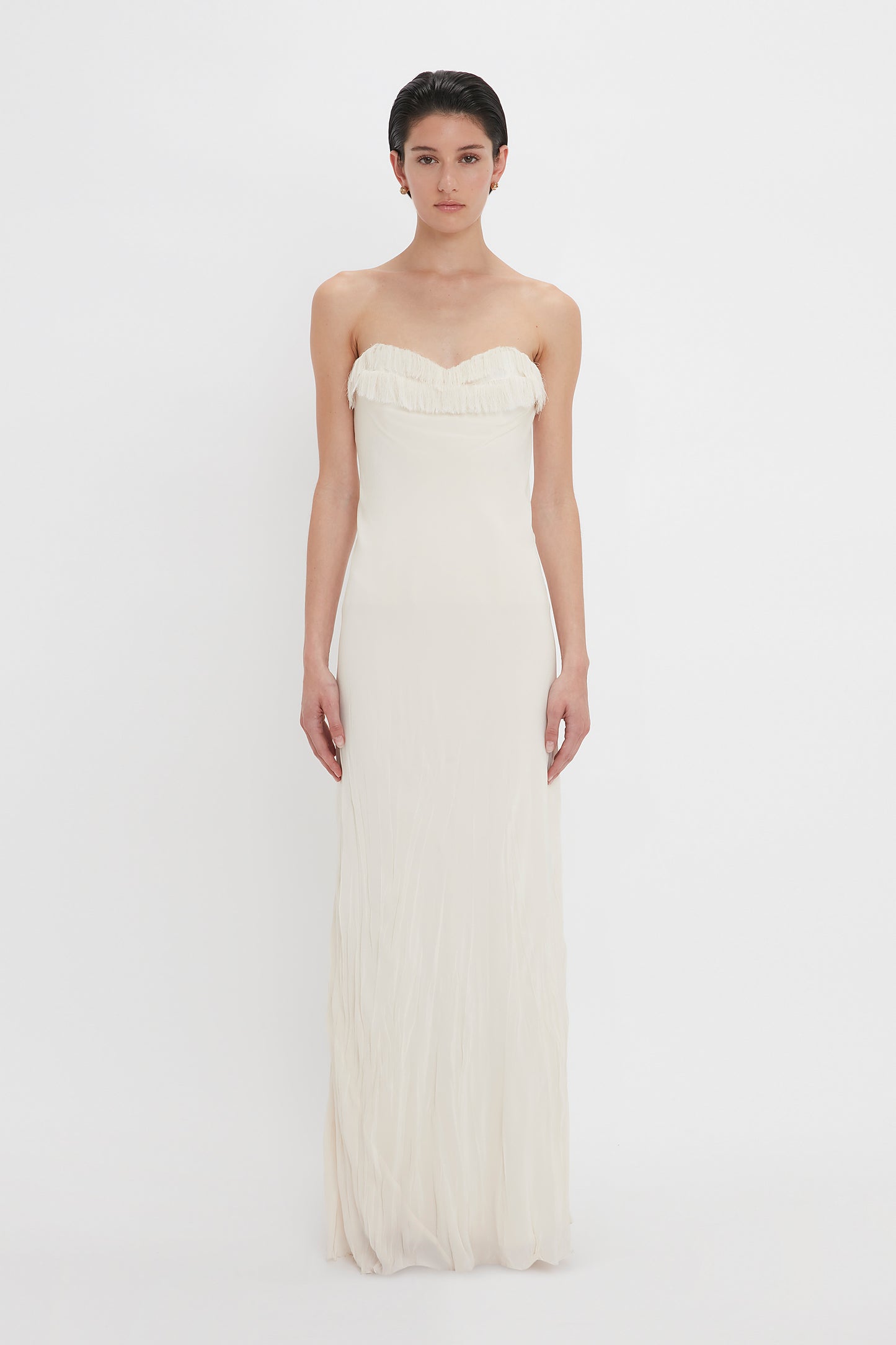 A woman in a Victoria Beckham Exclusive Floor-Length Corset Detail Gown In Ivory stands against a plain white background, looking directly at the camera.