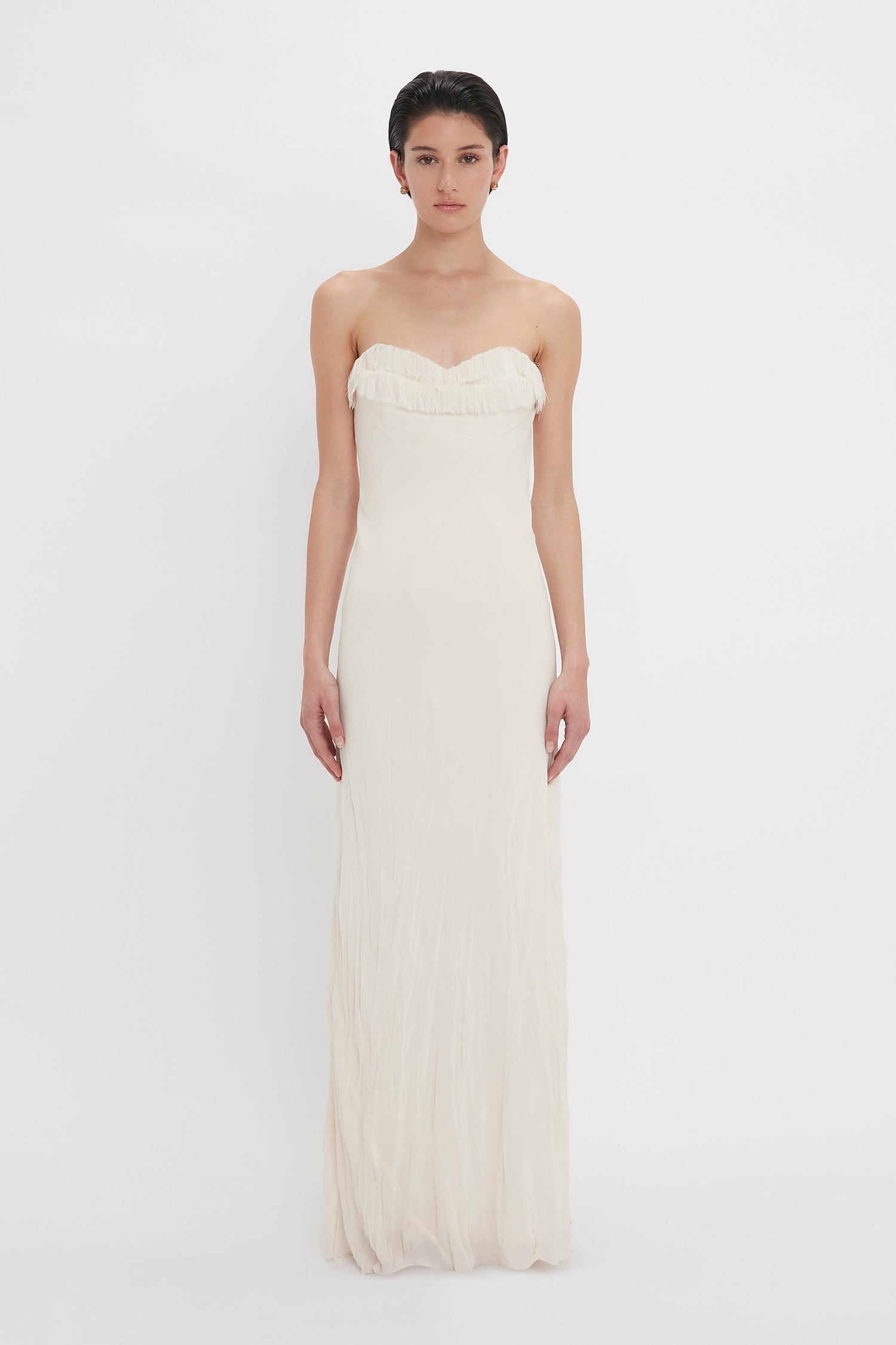 A woman in a Victoria Beckham Exclusive Floor-Length Corset Detail Gown In Ivory stands against a plain white background, looking directly at the camera.
