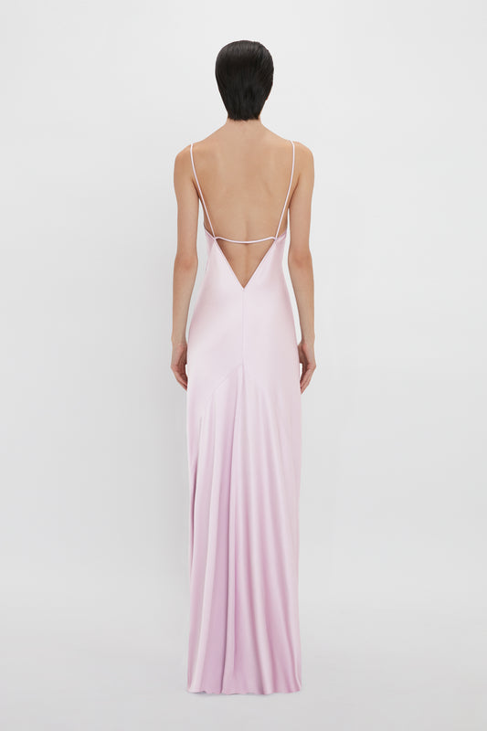 A woman viewed from behind, wearing an elegant, pastel pink Low Back Cami Floor-Length Dress In Rosa with thin straps and a low-cut back on a plain white background by Victoria Beckham.