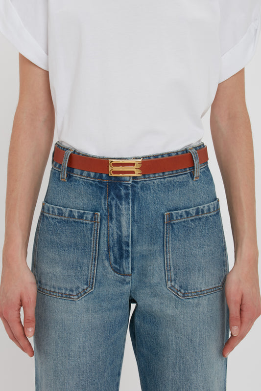Person wearing blue jeans and a white t-shirt, detailed with a Victoria Beckham Exclusive Frame Buckle Belt in Tan Leather featuring gold hardware.