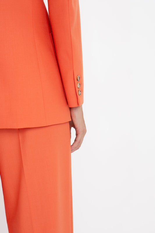 Close-up of a person wearing a Victoria Beckham Patch Pocket Jacket In Papaya with decorative buttons on the sleeve, standing against a white background.