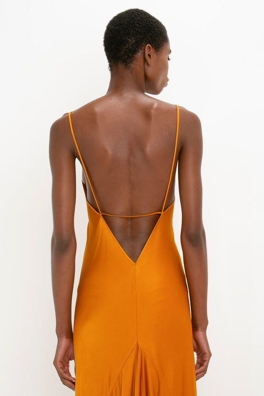 A woman viewed from the back, wearing an elegant, deep yellow Floor-Length Cami Dress in Ginger with a low-cut, crisscrossed back design by Victoria Beckham.