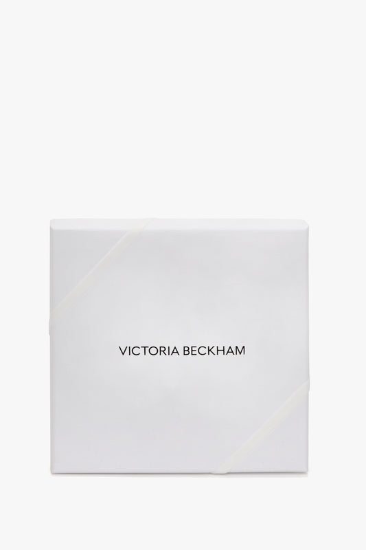 White gift box with a light ribbon, labeled "Victoria Beckham" in black font, featuring Exclusive VB Monogram Lace Tights In Black design, isolated on a white background.