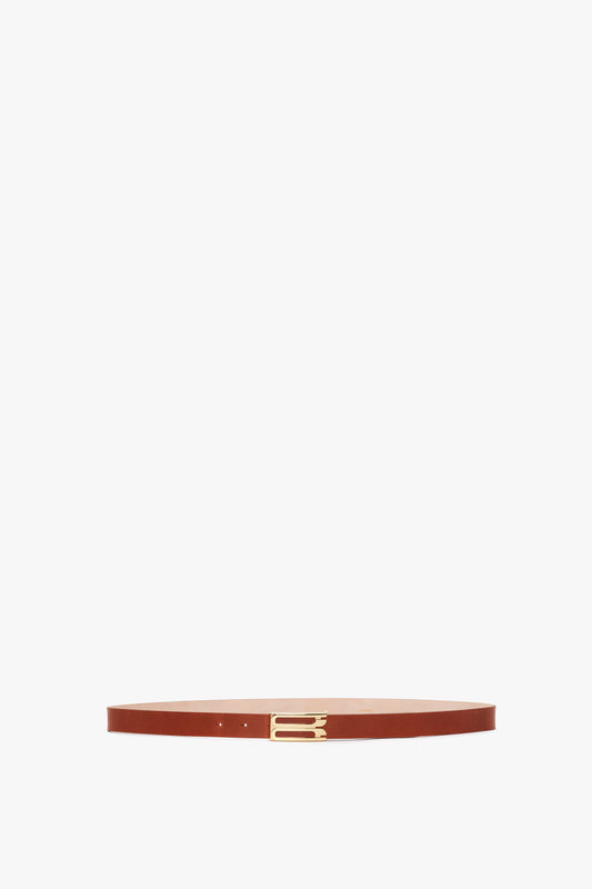 A slim, brown calf leather Exclusive Frame Buckle Belt In Tan Leather with gold hardware, displayed against a white background by Victoria Beckham.