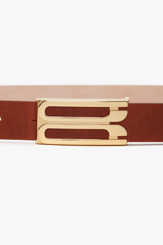 Close-up of a brown calf leather Exclusive Frame Buckle Belt In Tan Leather with a sleek, gold-colored buckle, set against a white background from Victoria Beckham.