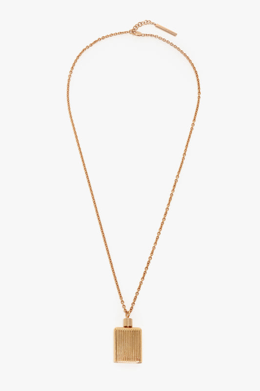 A gold brushed brass chain necklace with a rectangular pendant featuring vertical grooves, reminiscent of the elegance found in Victoria Beckham Exclusive Perfume Bottle Necklace In Brushed Gold.