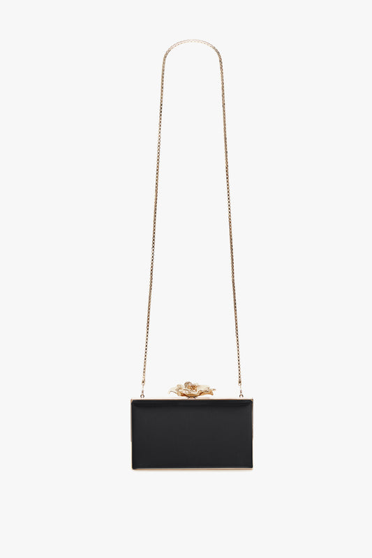 A black rectangular Victoria Beckham Frame Flower Minaudiere with a gold chain strap and a decorative gold frog on top, isolated on a white background.