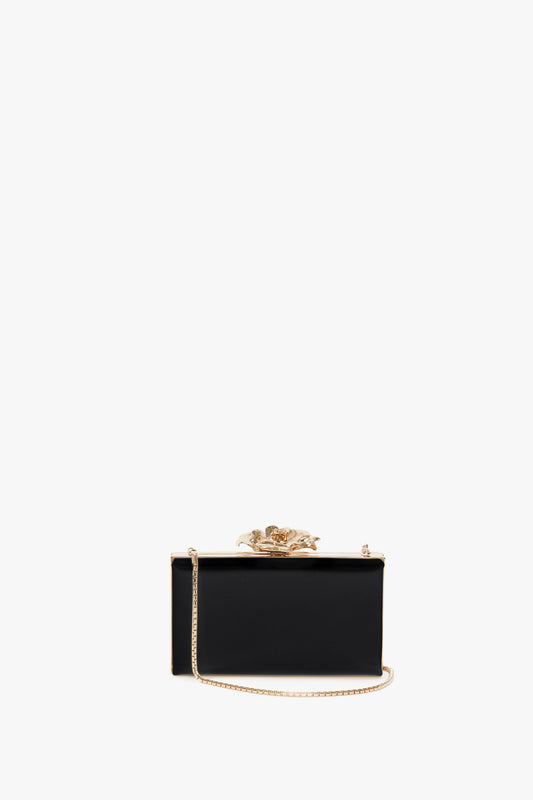 A Victoria Beckham black Frame Flower Minaudiere with a gold flower clasp and chain on a white background.