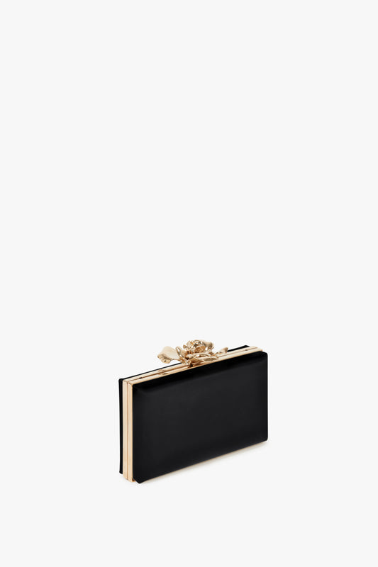 Elegant Frame Flower Minaudiere in Black clutch by Victoria Beckham with gold trim and a flower clasp on a white background.