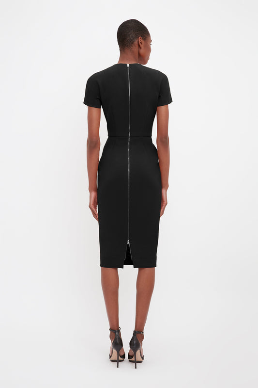 A woman standing, seen from the back, wearing a Victoria Beckham fitted black knee-length T-shirt dress made of bonded crepe fabric and Pointy Toe Stiletto Sandals.