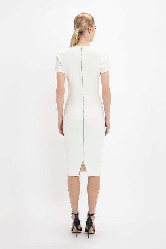 Woman in a Victoria Beckham fitted T-shirt dress in ivory with a back zipper, seen from behind, standing against a white background.