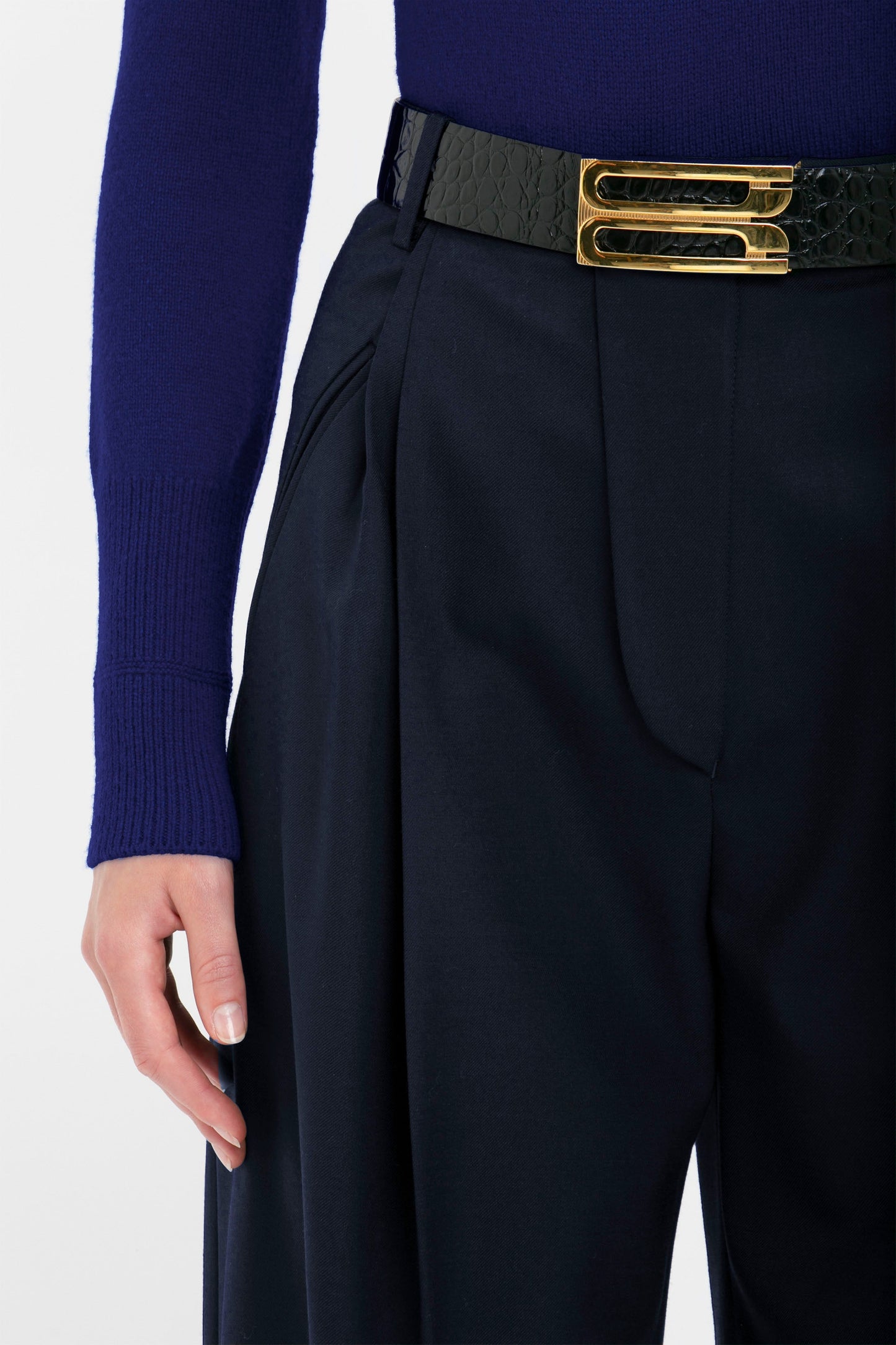 Close-up of a person wearing a Victoria Beckham Polo Neck Jumper In Navy, dark trousers, and a black belt with a gold double buckle. Only the torso and one arm are visible.