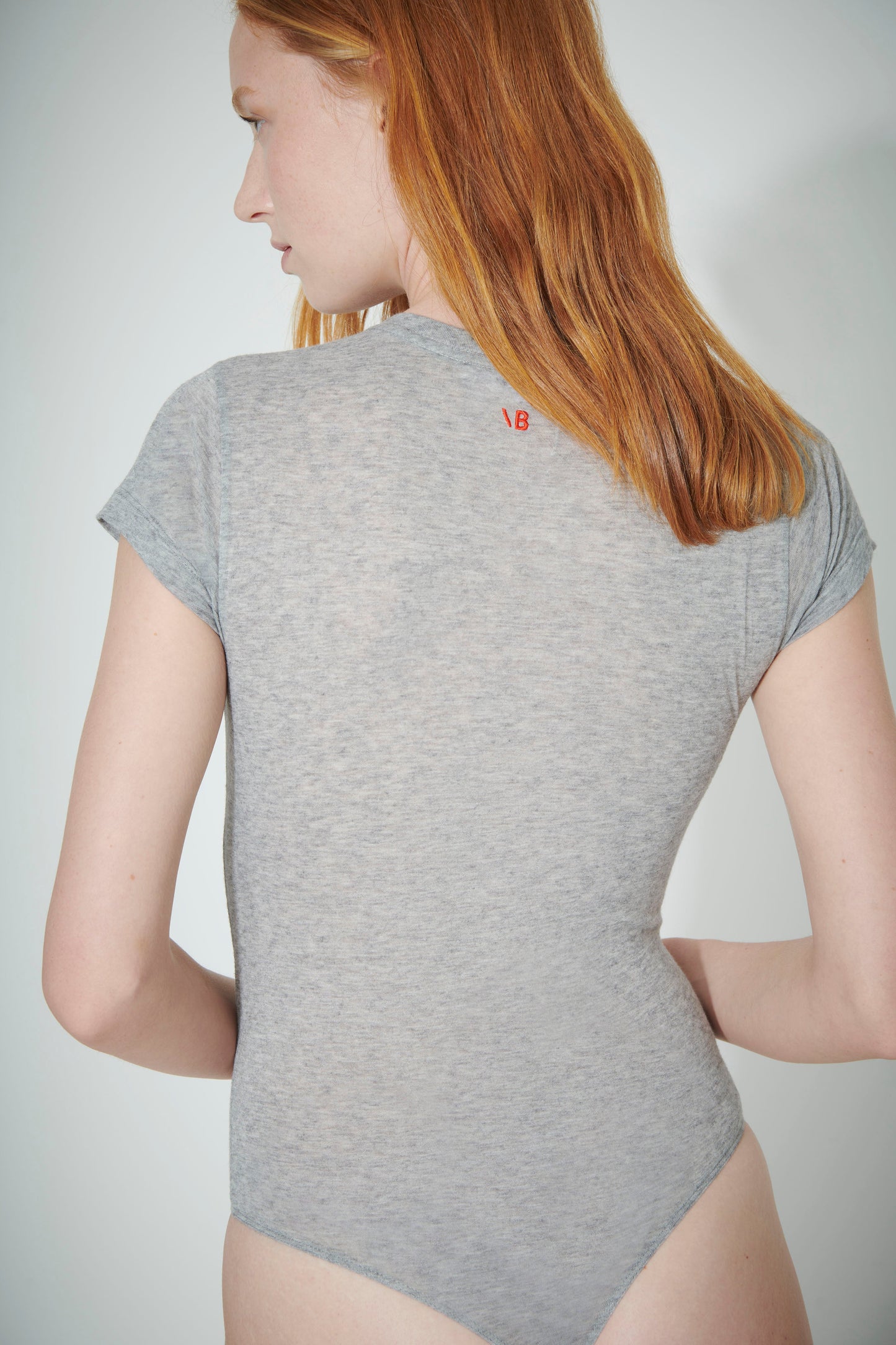 A person with long red hair facing away, wearing a Victoria Beckham T-Shirt Bodysuit in Grey, perfect as a layering piece.