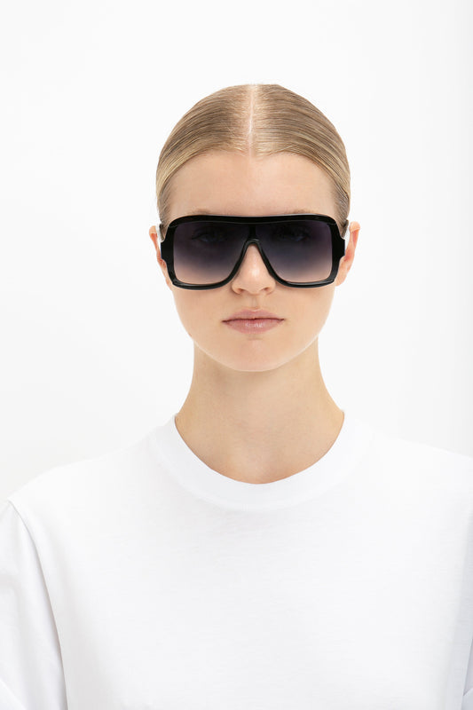 Woman with slicked-back hair wearing Victoria Beckham's Layered Mask Sunglasses In Black Gradient and a white crew-neck shirt against a plain white background.