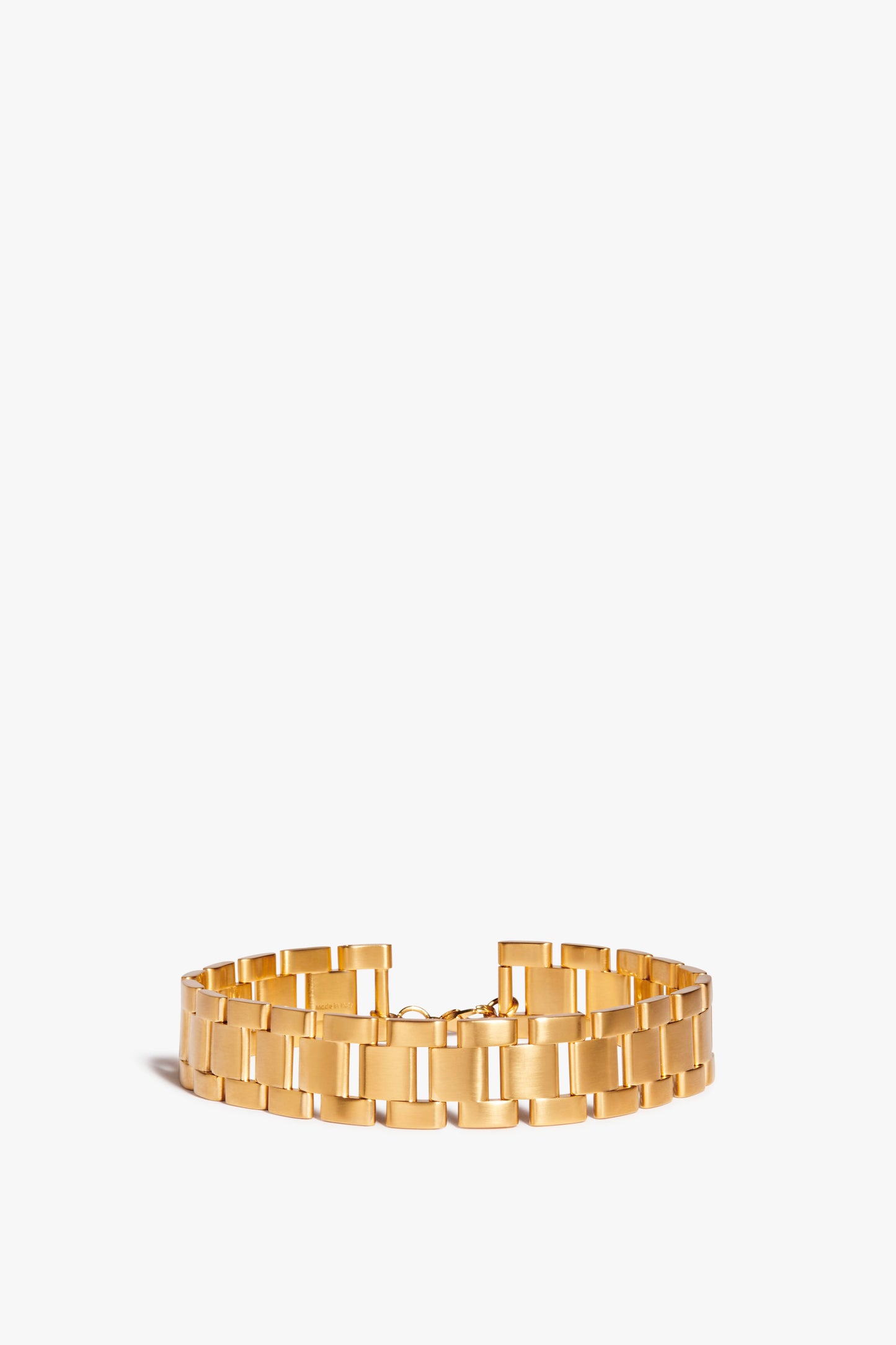 A Victoria Beckham Watch Chain Choker In Gold, reminiscent of a watch-inspired chain, features a broad, flat, and shiny surface against a plain white background.
