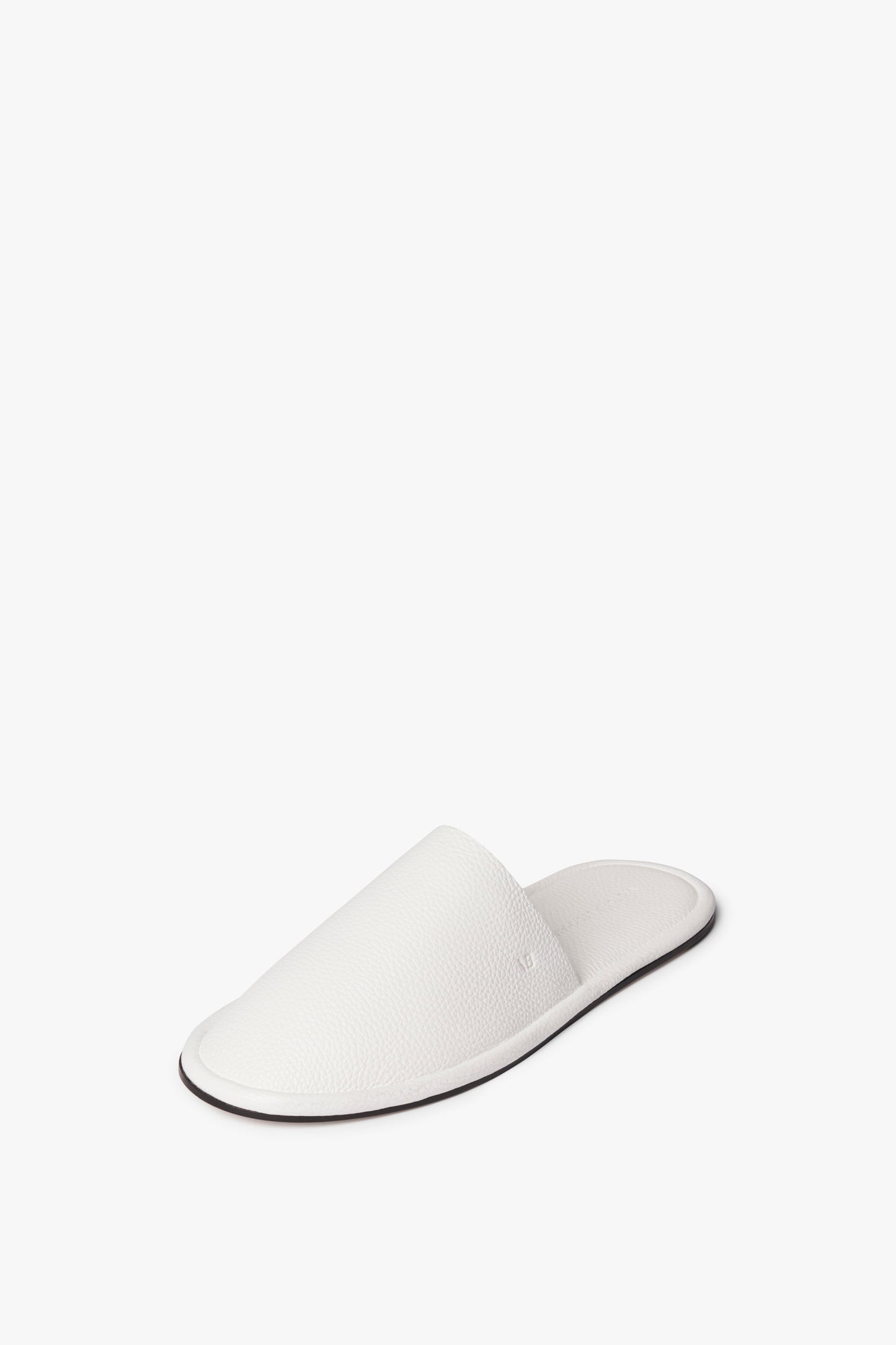 The Victoria Beckham Amelia Leather Mule in White is a chic outdoor slip-on shoe made from embossed leather fabrication, featuring a single white slipper with a closed toe and open back, displayed on a white background.