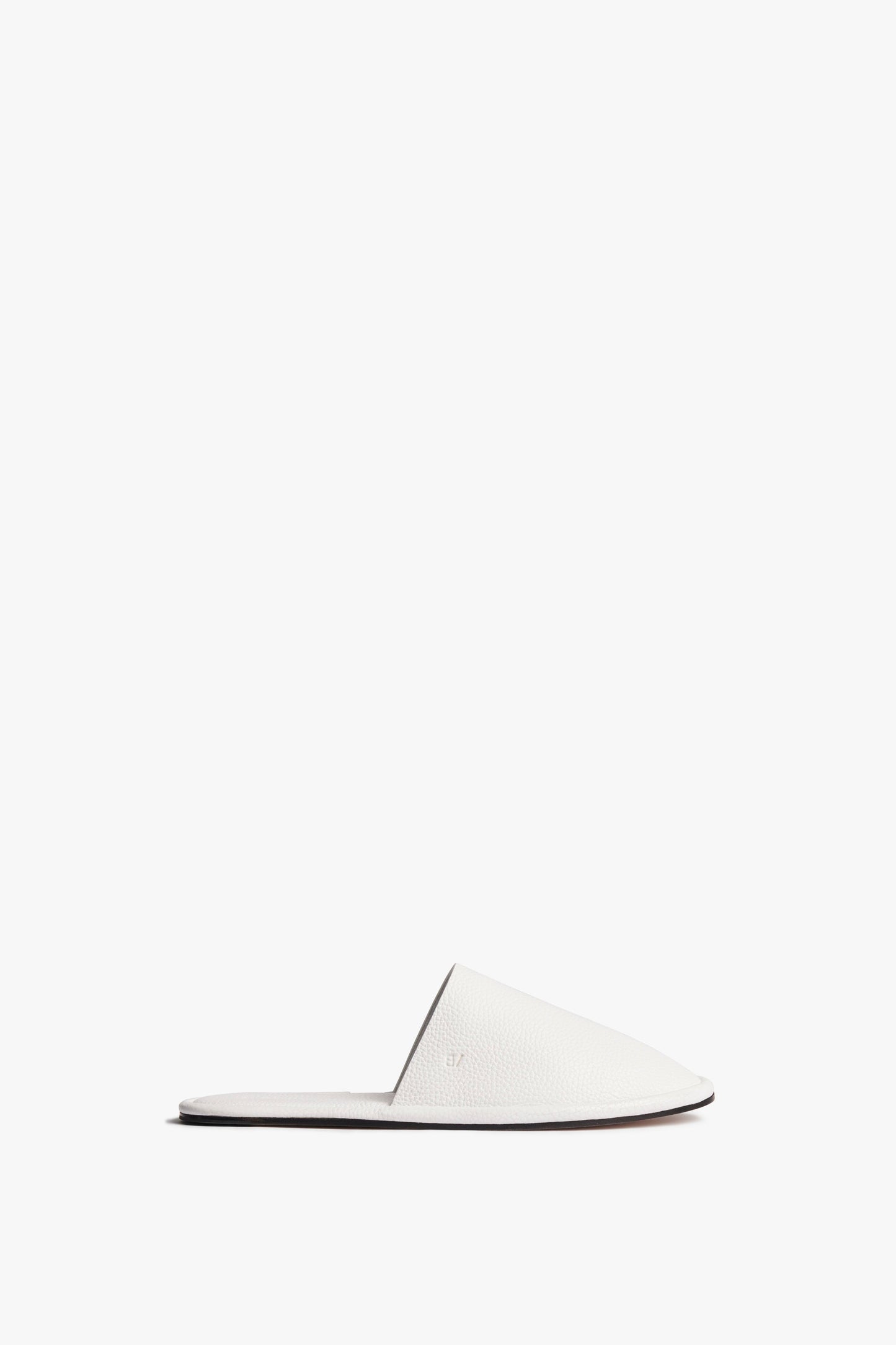 The Victoria Beckham Amelia Leather Mule in White, an outdoor style slip-on shoe, features a white, minimalist design with an open back and flat sole. Displayed against a plain white background, its elegance is enhanced by the embossed leather fabrication.