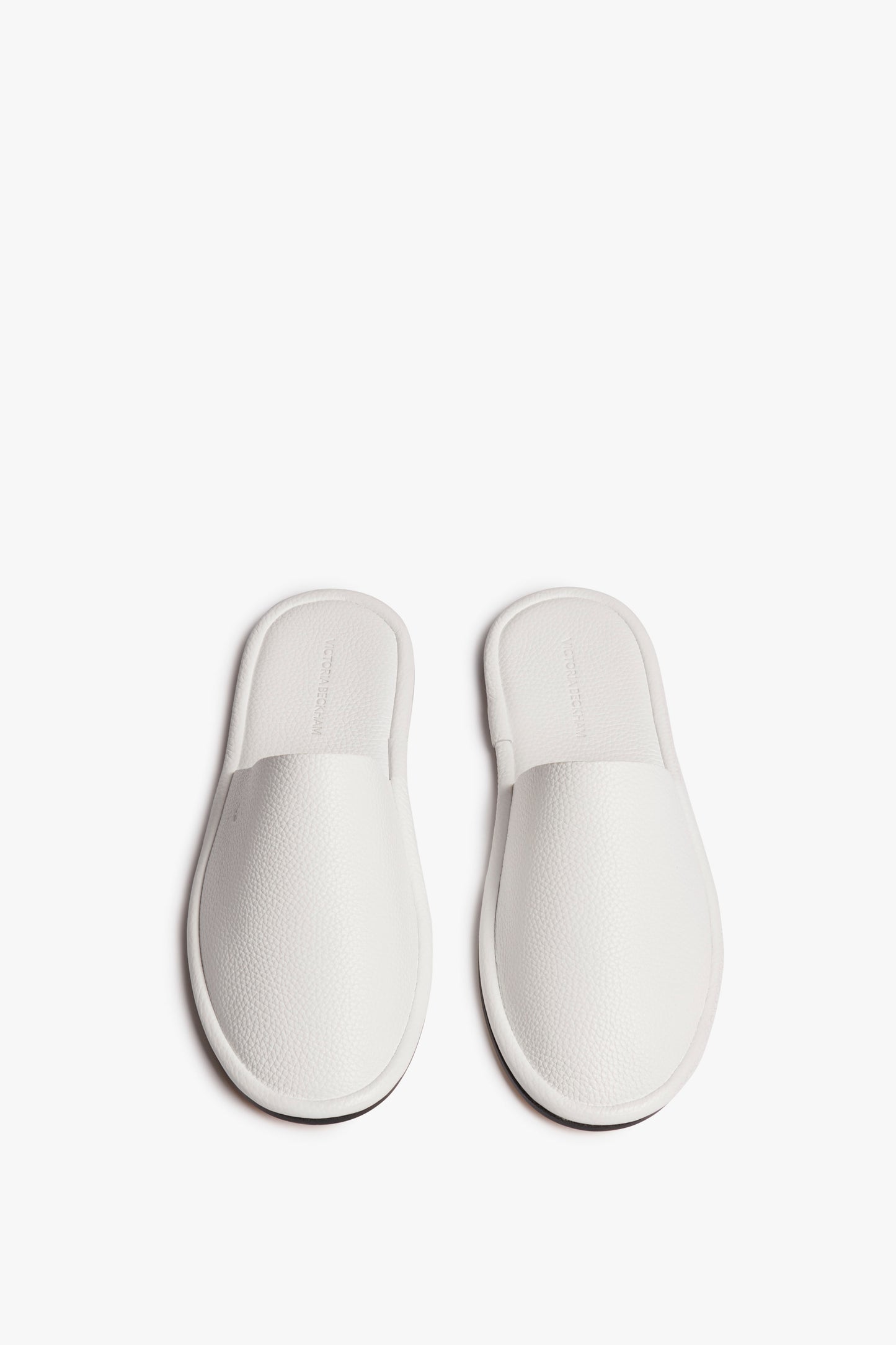A pair of white Victoria Beckham Amelia Leather Mule in White slip-on house slippers with a textured surface, viewed from above against a white background.