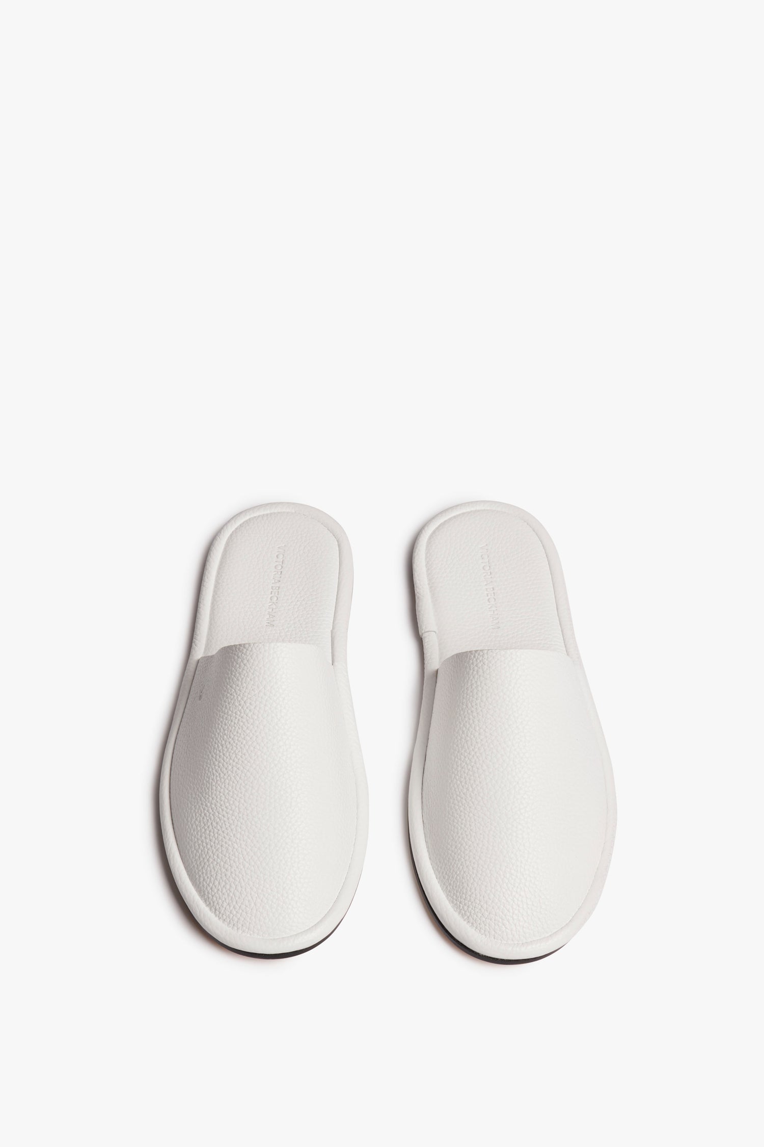 A pair of white Victoria Beckham Amelia Leather Mule in White slip-on house slippers with a textured surface, viewed from above against a white background.