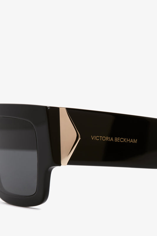 Close-up of the side arm of Victoria Beckham V Plaque Frame Sunglasses in Black showcasing the logo and angular gold-tone metal detail.