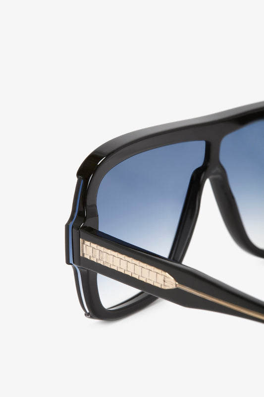 Close-up of Victoria Beckham black sunglasses with black lenses and a textured metal detail on the temples, against a white background.