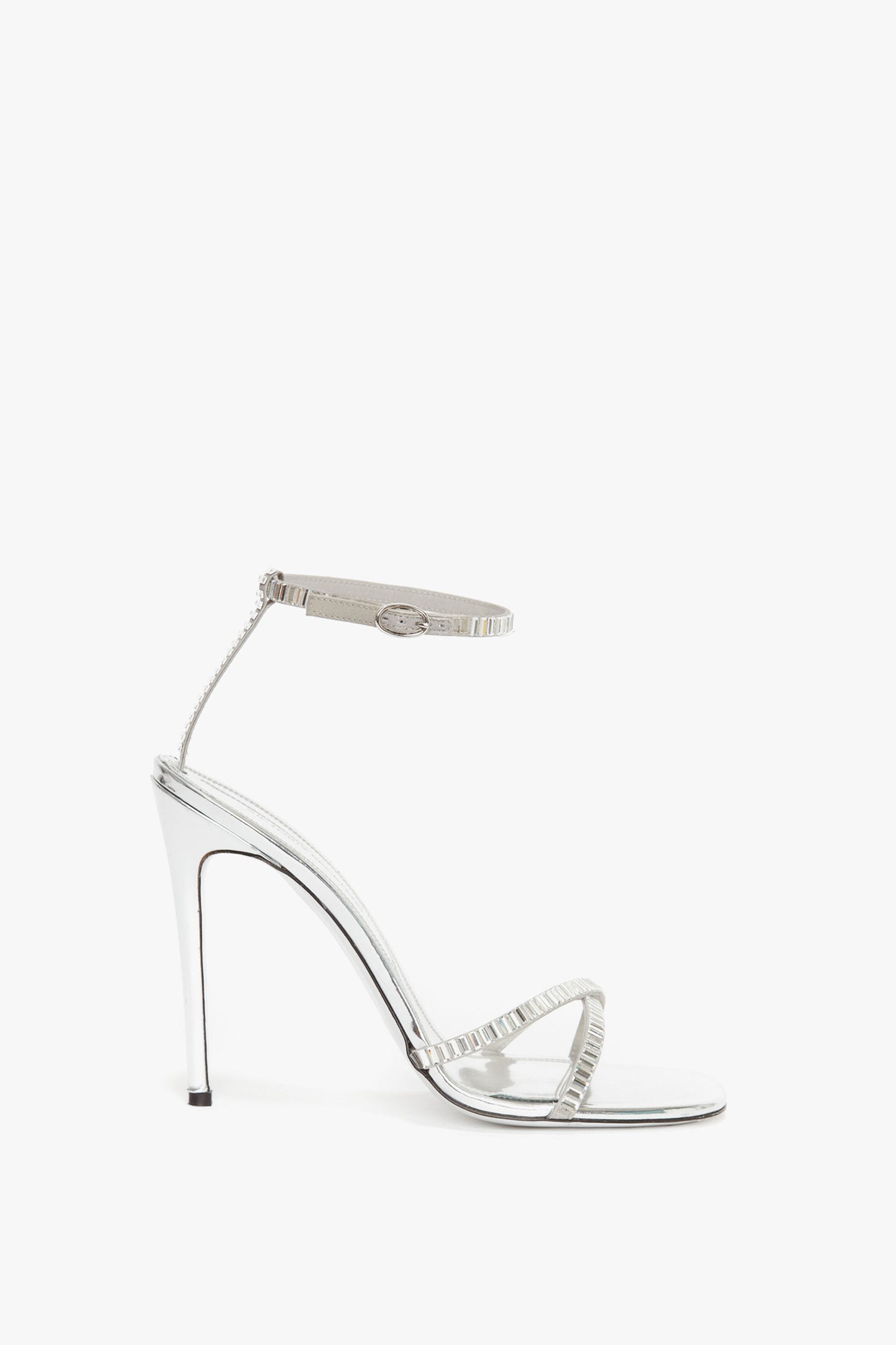 A Victoria Beckham Rhinestone Sandals In Silver made of metallic silver leather, featuring a sleek ankle strap and delicate straps across the toes, viewed from the side.